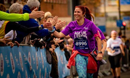 Woman giving high fives to the crowd whilst running in the ž Leeds Abbey Dash